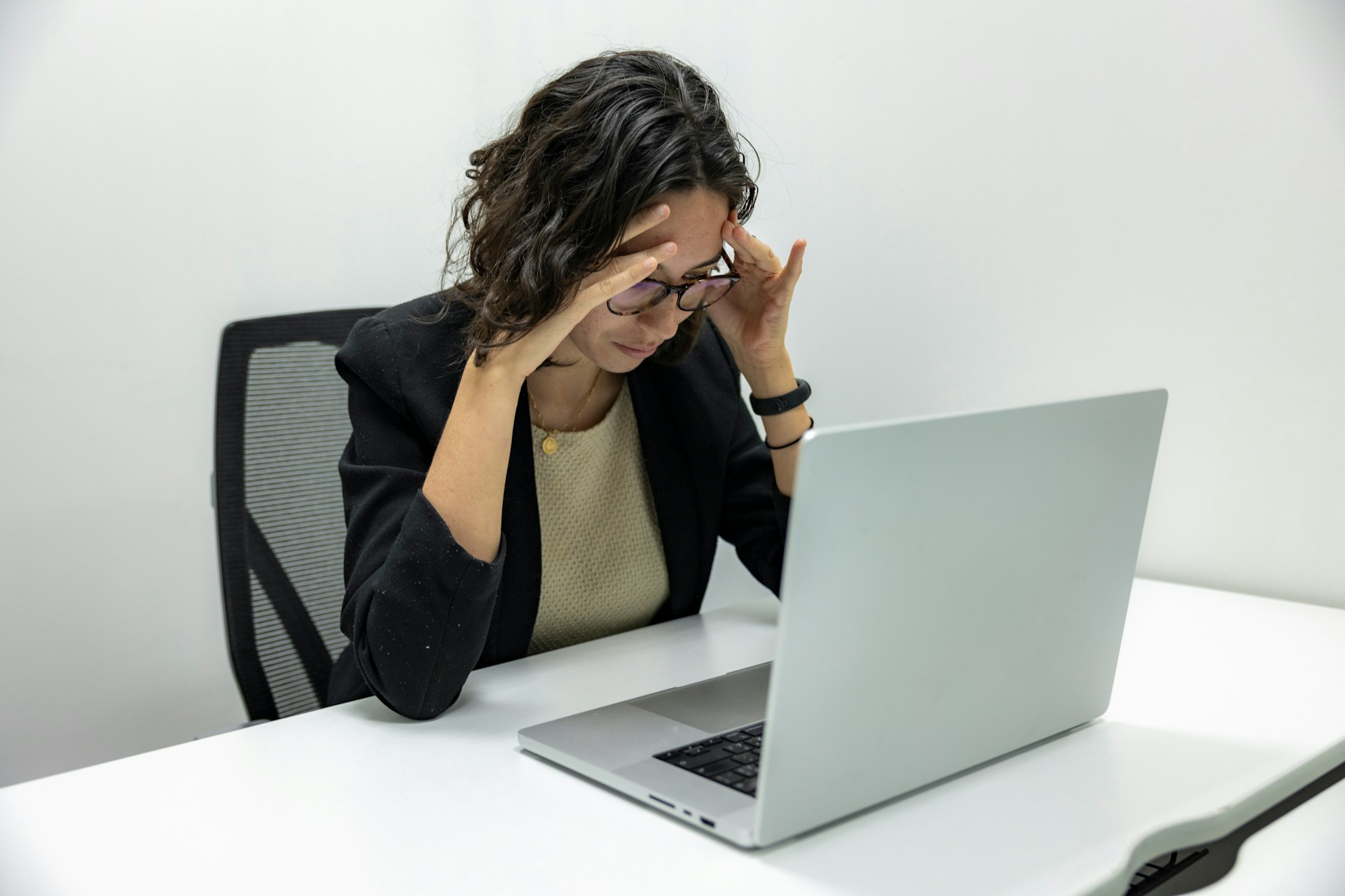 A stressed woman in a blazer sits at a desk